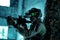 Man in uniform with machine gun and turned on night vision device beside brick wall. Airsoft soldier with green light on face in