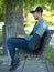 Man using computer with wireless earbuds on a park bench