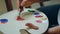 A man is using a flat brush to mix two colours on a palette and paint onto a canvas