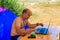 Man using his laptop sitting at a folding picnic table in a camping. Working while traveling. Freelance work