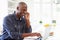 Man Using Laptop And Talking On Phone In Kitchen At Home