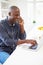 Man Using Laptop And Talking On Phone In Kitchen At Home