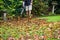 A man using a leaf blower machine to clear autumn leaves from a garden during fall