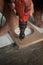 A man using powered drill with a hole saw bit to make precision hole in a wooden plank.