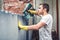 Man using protective gloves painting a grey wall with spray paint gun. Young worker renovating house