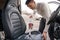 Man vacuuming car seat with vacuum cleaner in auto