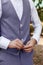 Man in Very Peri suit fastens the buttons of the jacket, close-up. Gentleman getting ready in the morning. Trendy color
