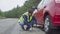 A man in a vest installs a jack to change a tire in a car. On the roadside