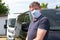 Man vip taxi driver in medical face hande made mask aside black van car looks at camera in concept of covid-19 coronavirus