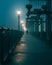 man walking across bridge on a foggy night with lamp post in foreground