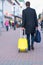 Man walking away pulling a yellow suitcase