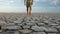 Man walking barefoot on bottom of dried lake, stepping on cracked soil ground