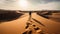 Man walking in the desert with footprints in the sand at sunset.