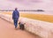 Man walking a dog with a read leashed harness along the promenade in winter at the seafront in Deal, Kent, Uk.