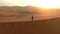 Man, walking and drone in desert or mountains of sand with sunset background. Person, travel and adventure for freedom