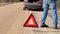 Man walking near warning triangle on the road near car