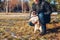 Man walking pug dog in snowy winter park. Master playing with pet holding it on hind legs. Activities with animals