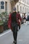 Man walking with red Scottish fabric cloak and black trousers before Versace fashion show, Milan