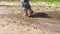 Man with walking stick walking barefoot through pool on an earth road at summer season