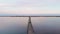 Man walking on wooden bridge through lake with calm clear water. Bridge over estuary in sunrise lights