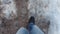 Man walks along a road not cleared of dirty snow, slush in winter. First-person view of own feet. Above-zero temperature