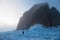 Man walks among blue ice around figured rocks in the fog