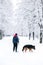 A man walks a German shepherd in a snowy park