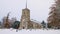 Man walks by a traditional English village church covered in snow. UK.