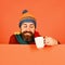 Man in warm hat holds white cup on orange background