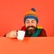 Man in warm hat holds white cup on orange background