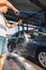 A man washes his car at a self-service car wash using a hose with pressurized water