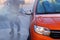 Man washes his orange car at car wash in outdoors. Cleaning with with a water jet at self-service car wash.