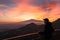 Man watching beautiful sunset behind volcano Mount Etna near Castelmola, Taormina, Sicily. Clouds with vibrant red orange colors