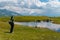 A man watching cows swimming in a pond near the Koruldi Lake with a dream like view on the mountain range near Mestia in the