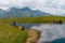 A man watching cows swimming in a pond near the Koruldi Lake with a dream like view on the mountain range near Mestia in the