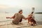 A man wear straw hat and playing guitar music song near the sea sunset and stroking the head dog pet