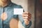 Man wearing blue jeans shirt and showing blank white business card. Blurred background. Horizontal mockup