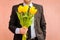 A man wearing a business suit, holding a bouquet of tulips. The man gives a bouquet of flowers