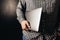 Man wearing casual clothes holds closed laptop, black blurred background