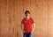 Man wearing Chinese Communist Party flag color shirt and standing with two hands in pant pockets on the wooden wall background