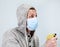 Man wearing hoodie and medical facial mask holding spray cleaner in hand, a grey background