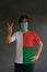 Man wearing hygienic mask and wearing Madagascar flag colored shirt and raising two fingers up on dark wall background