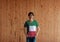 Man wearing Kuwait flag color shirt and standing with two hands in pant pockets on the wooden wall background