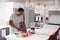 Man Wearing Pyjamas Standing In Kitchen Chopping Fruit And Vegetables For Fresh Smoothie