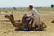 Man wearing turban and traditional dress gets his camel ready for a safari ride in the desert near Jodhpur, India.