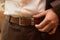 Man wears belt. Close-up of male waist with hand on brown leather belt