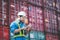 Man wears hardhat and reflection shirt and checking tablet with blurry metal containers in background. Concept of inventory and