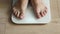 Man weighing himself - male bare feet stepping on white digital floor scales at home: close up view. Measuring weight