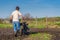 Man in wellingtons with cultivator ploughing ground in sunny day. Farmer plowing kitchen-garden in suburb. Land cultivation, soil