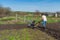 Man in wellingtons with cultivator ploughs ground in sunny day. Land cultivation, soil tillage. Spring work in garden. Gardening